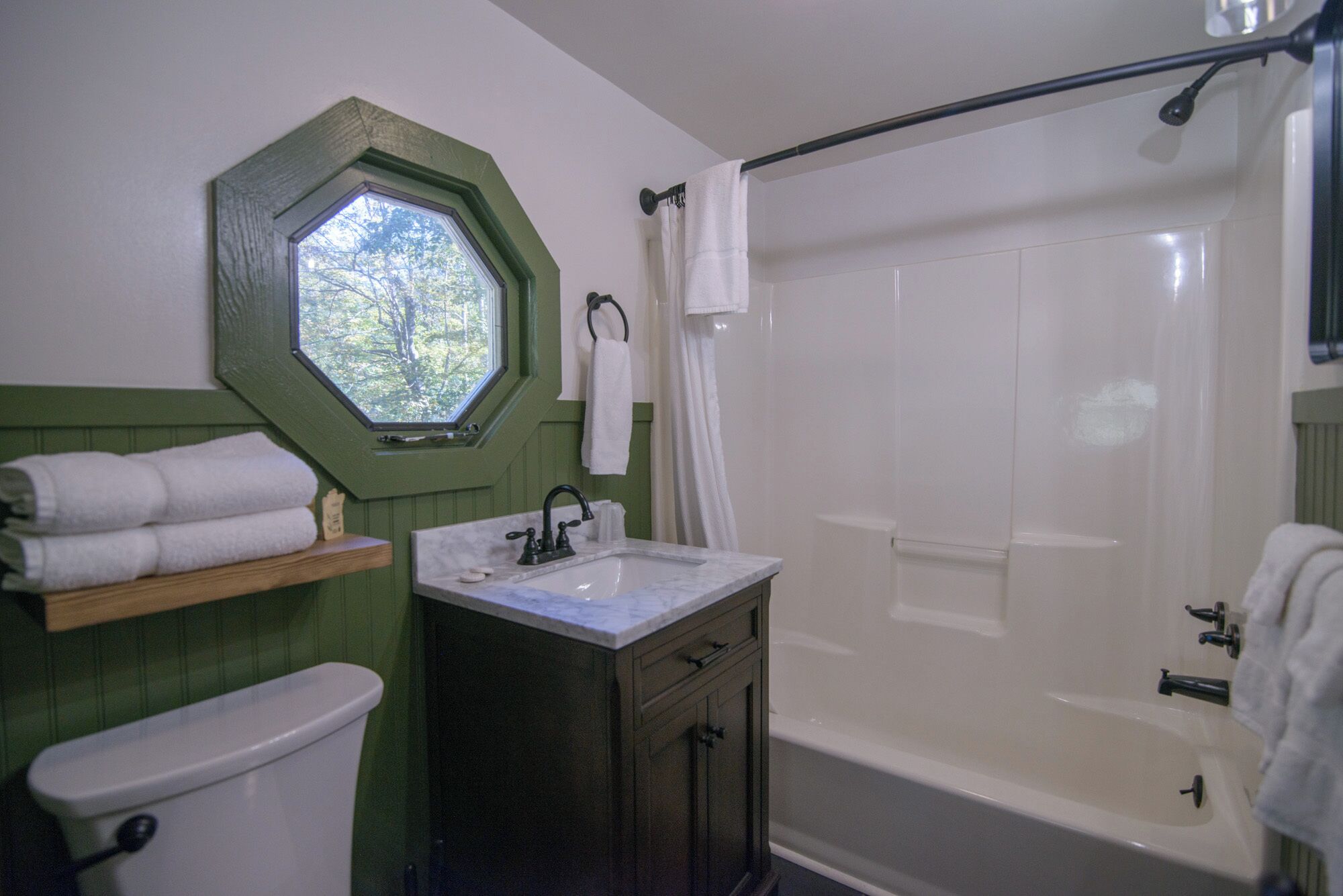 Een badkamer met toilet, wastafel en bad. Er is een raam boven de wastafel en een handdoekrek met handdoeken.