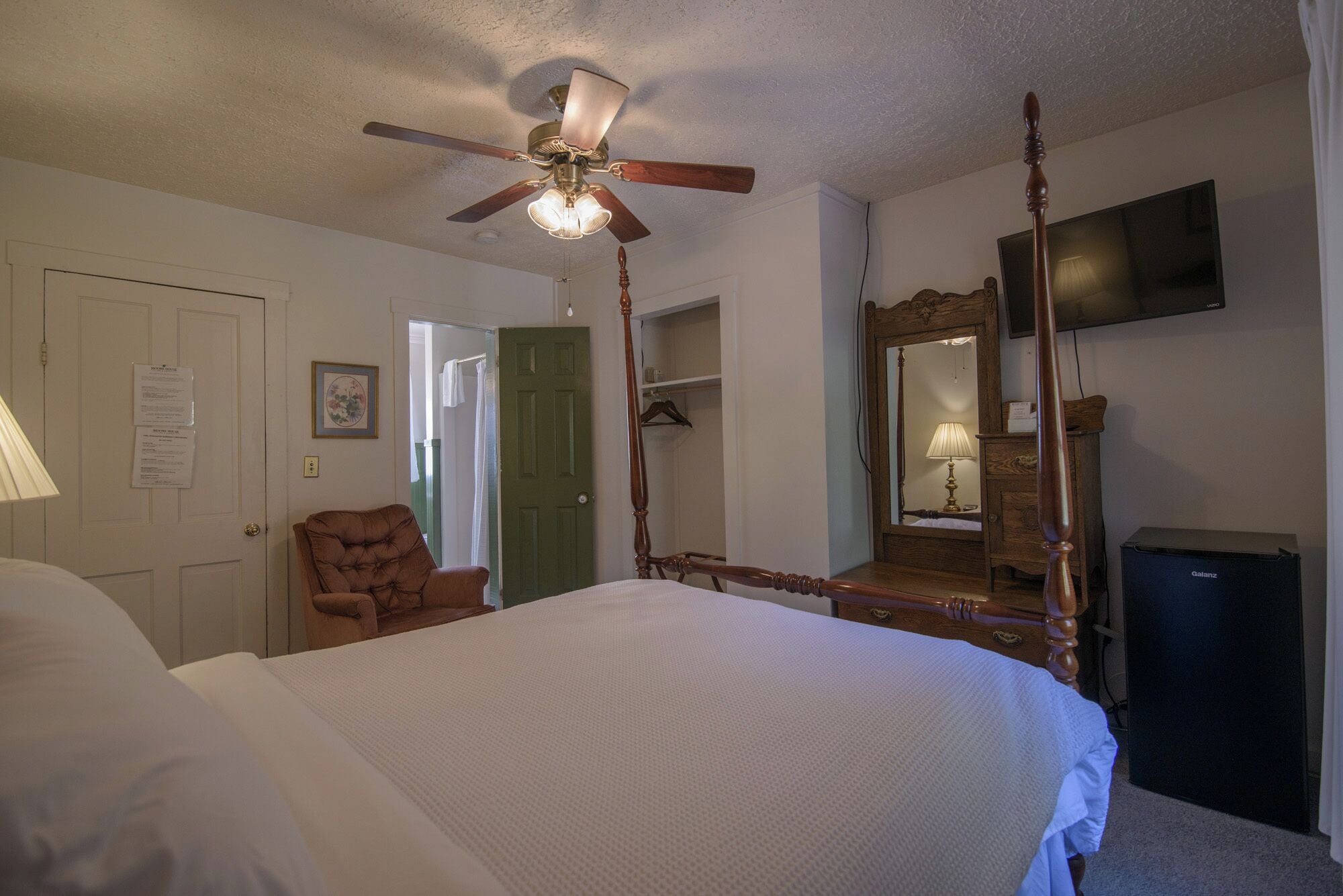 Une chambre à coucher avec un lit à baldaquin, un ventilateur de plafond, une commode en bois, un miroir et un téléviseur.