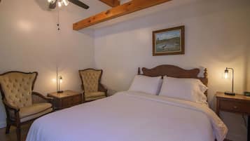 Ein Schlafzimmer mit einem großen Bett, zwei Polsterstühlen, einem Deckenventilator und einem Gemälde an der Wand.