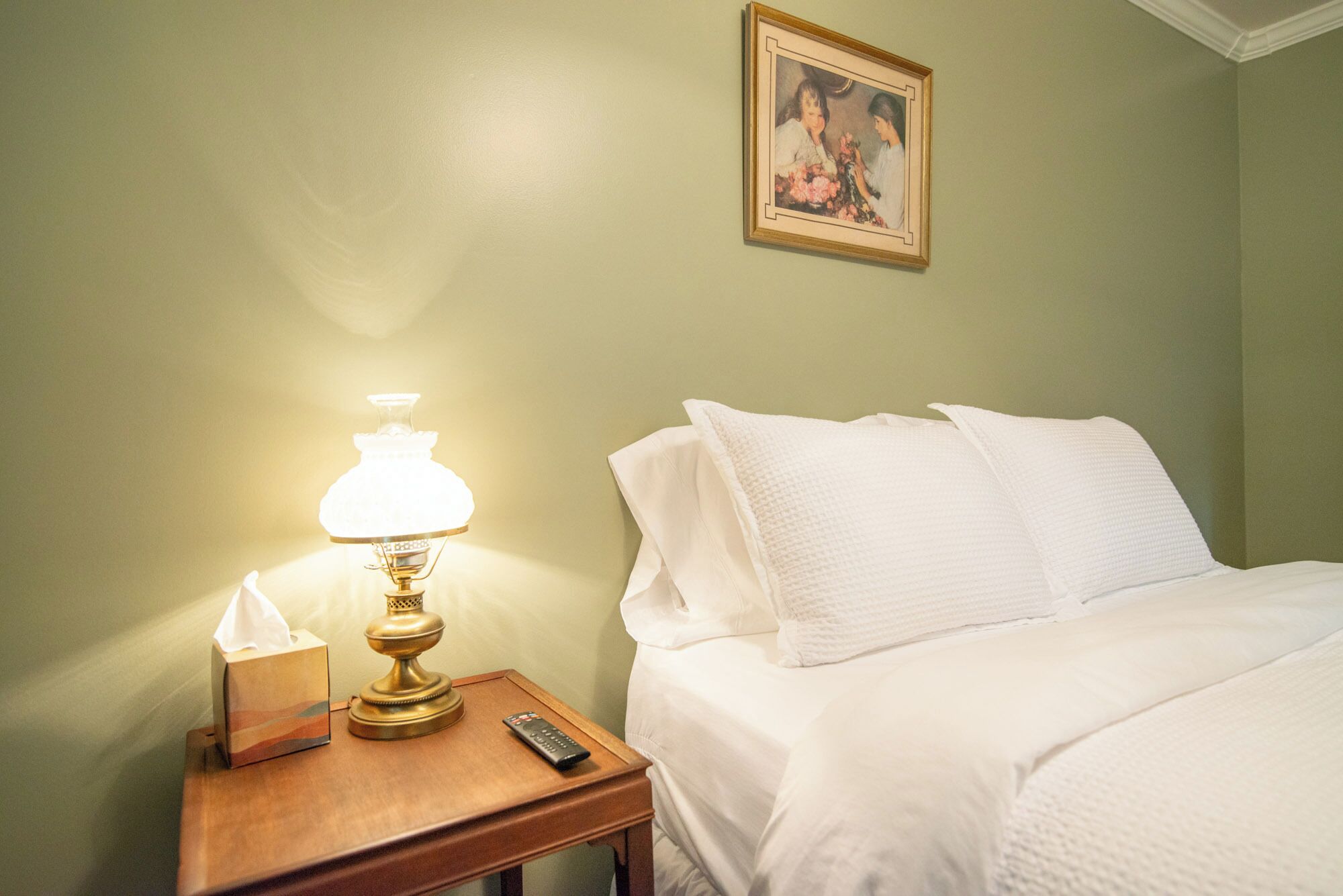 A hotel room with a bed, a nightstand with a lamp, a remote control, and a tissue box.