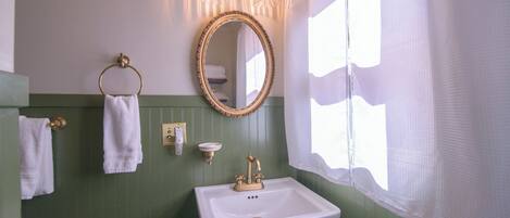 Une salle de bain avec un mur vert, un lavabo blanc, un miroir encadré d’or et un porte-serviettes.