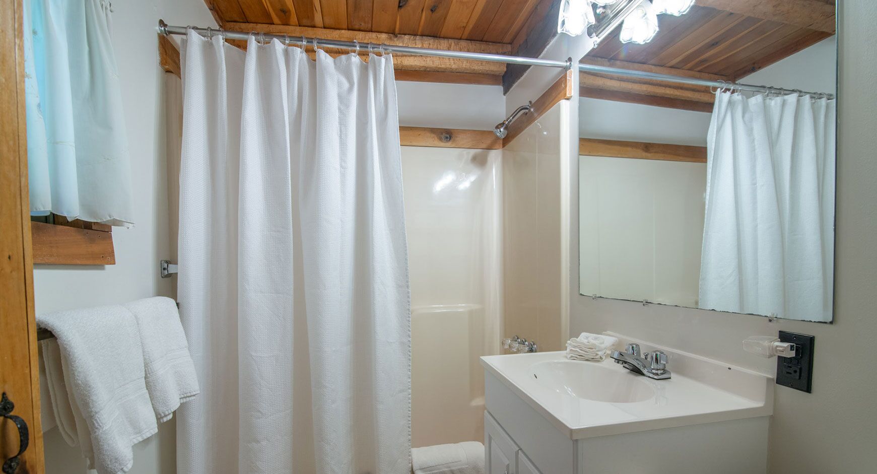 Un bagno con tenda doccia, lavandino, specchio e portasciugamani.