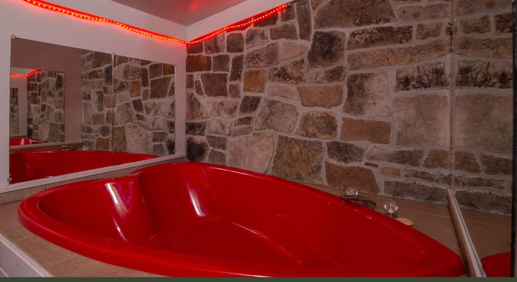 A bathroom with a red bathtub, stone walls, and a mirror.