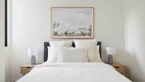Un lit bien fait, avec une literie blanche, deux tables de chevet avec des lampes et une œuvre d’art encadrée au-dessus du lit.