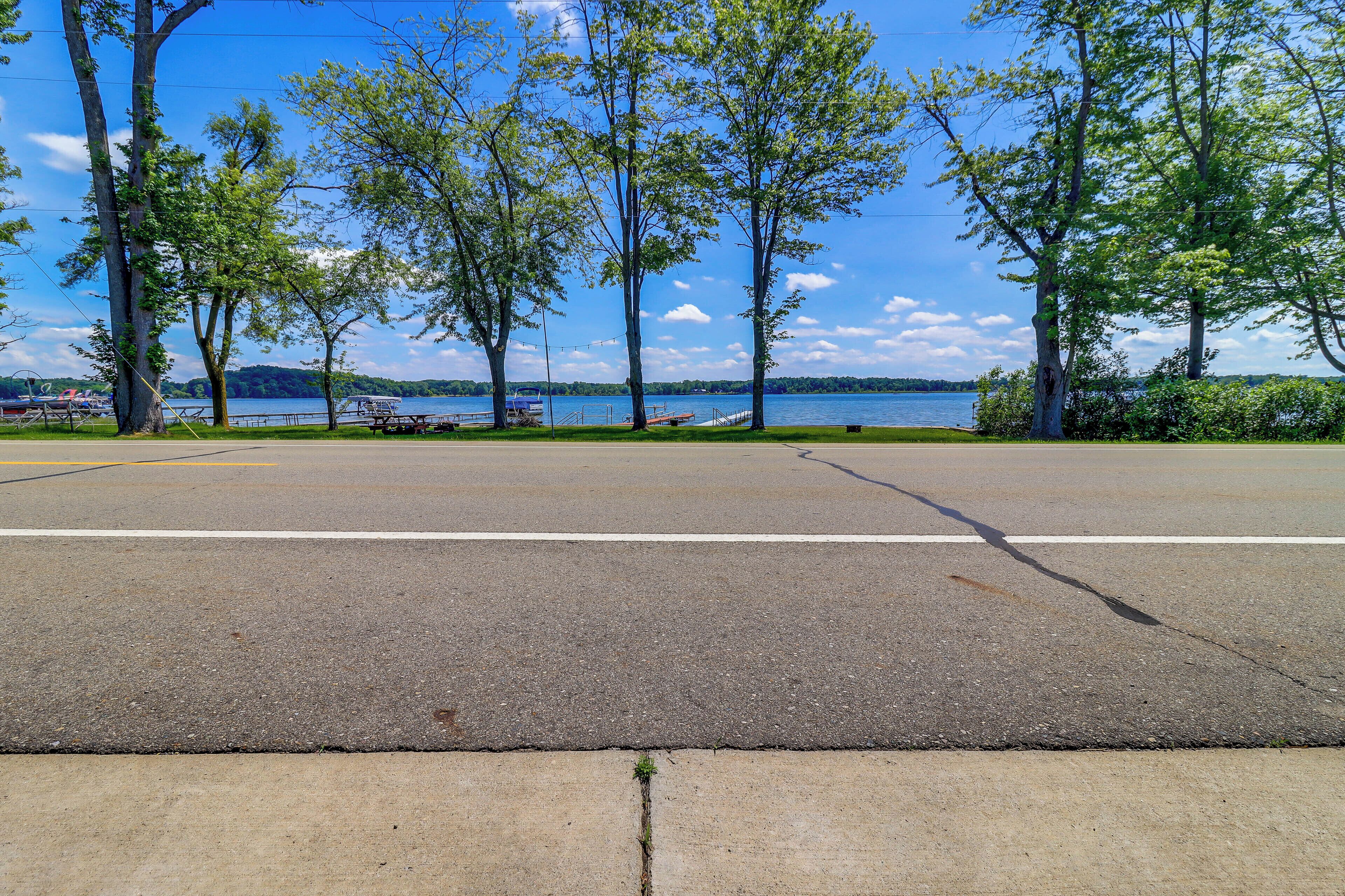 A parking lot with a concrete divider and a grassy area with trees and a lake in the background.