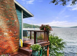 A wooden deck with a railing, a chair, and a potted plant with an American flag. - Winnipesaukee Lakefront Cabin w/ Private Dock Slip (Laconia)
