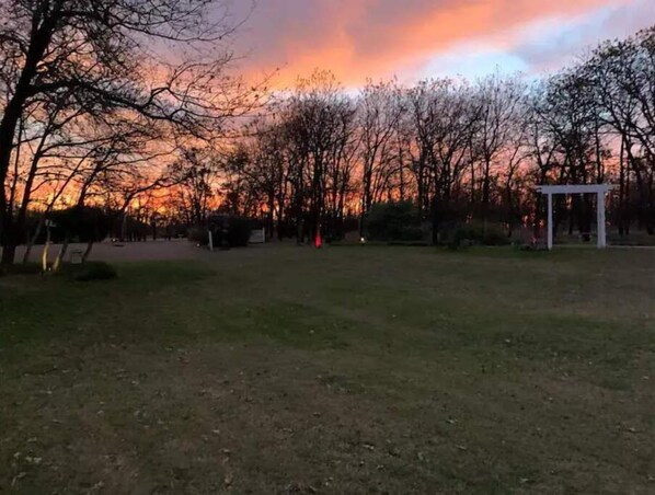 A park with a white gazebo, trees, and a sunset in the background.