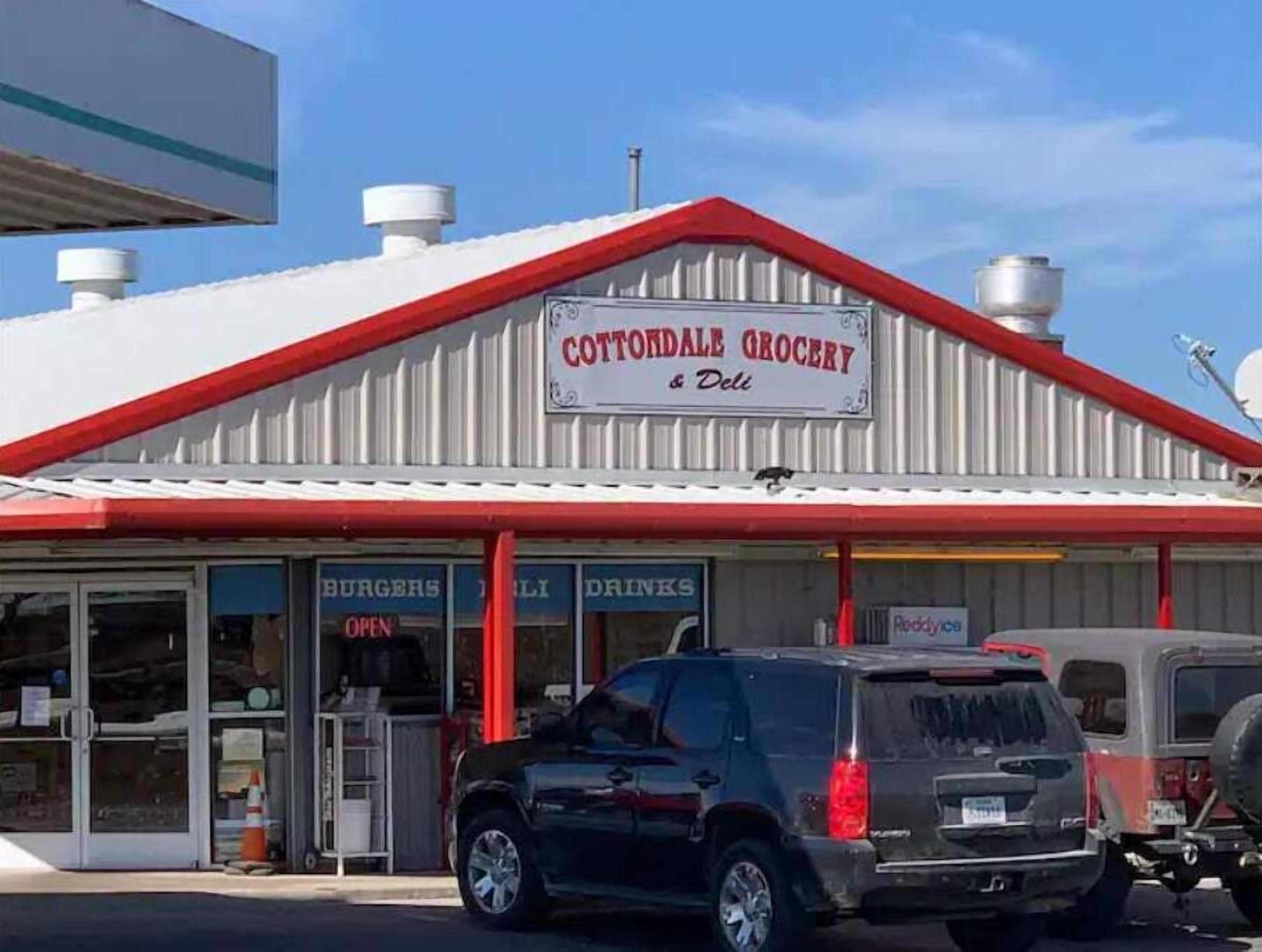 Ein Geschäft mit einer Beschilderung mit dem Schriftzug "Cottondale Grocery & Deli“, mit rotem Dach und weißen Wänden.