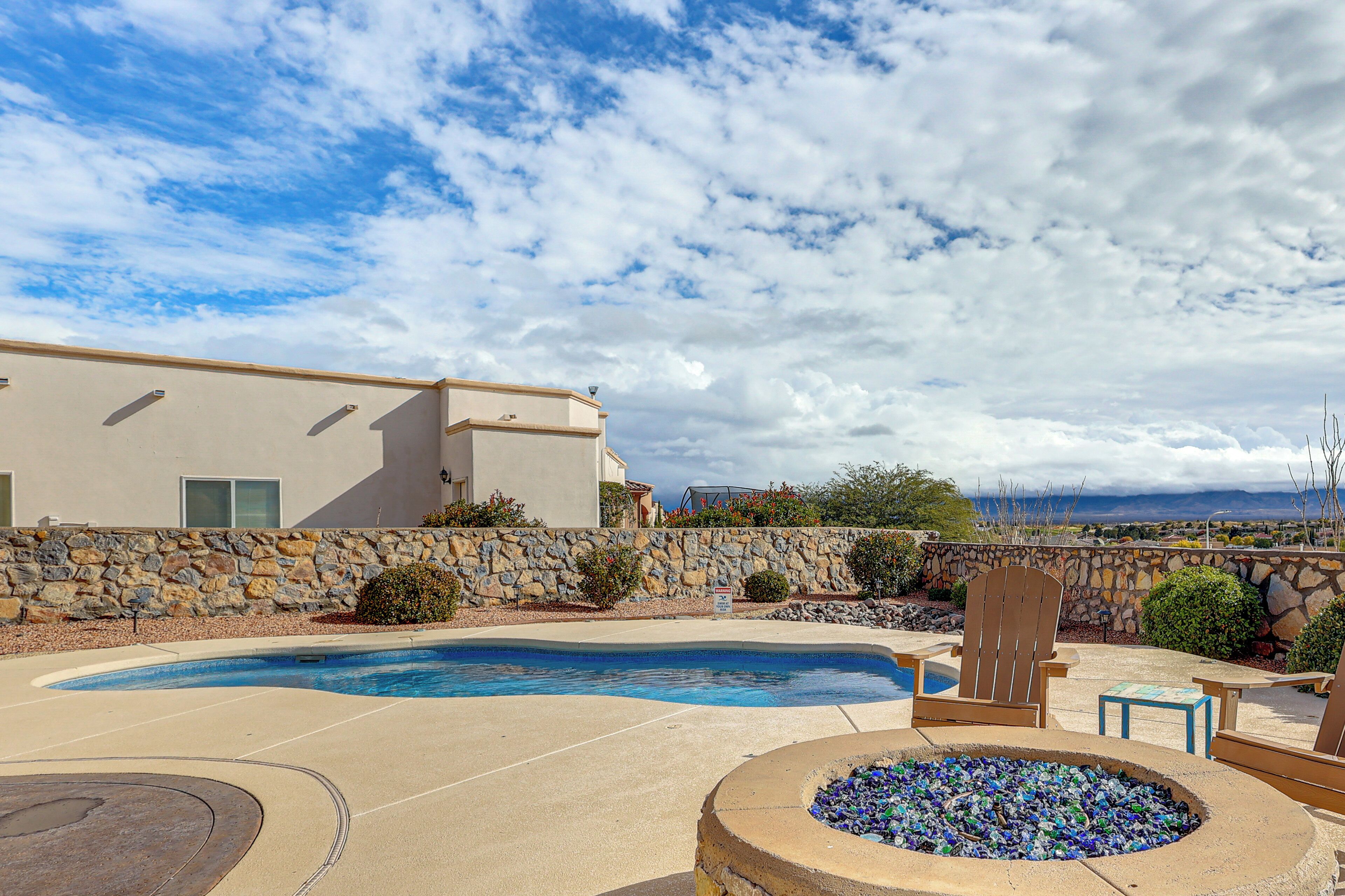 A swimming pool with a stone wall, a fire pit, and outdoor seating.