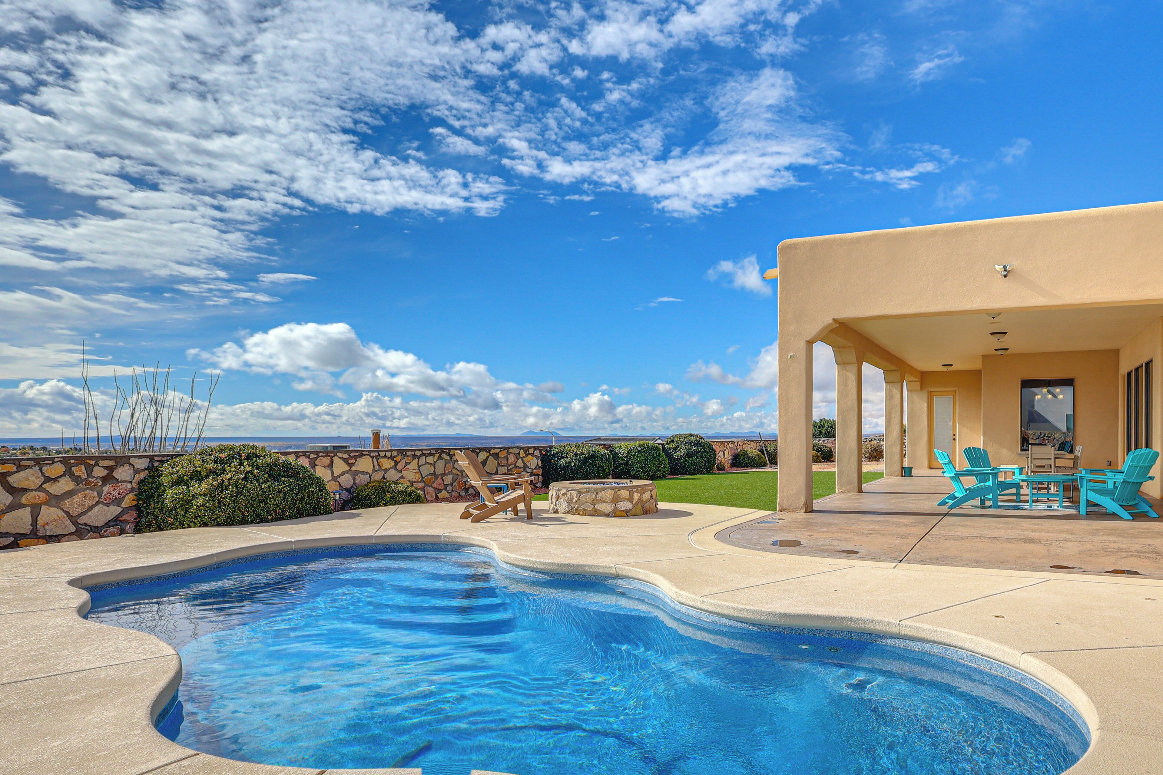 A swimming pool with a stone wall and a patio area with chairs and a table.