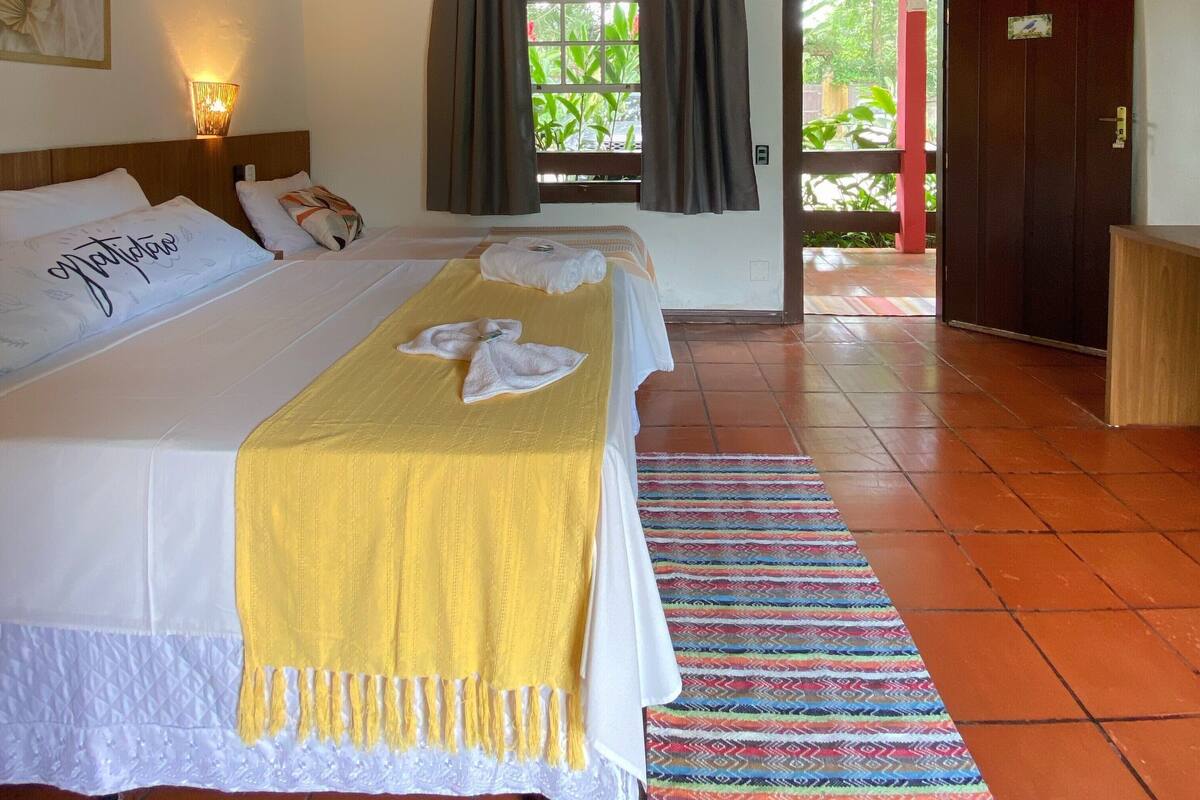 A hotel room with two beds, a ceiling fan, a window with curtains, a wooden door, and a colorful rug.