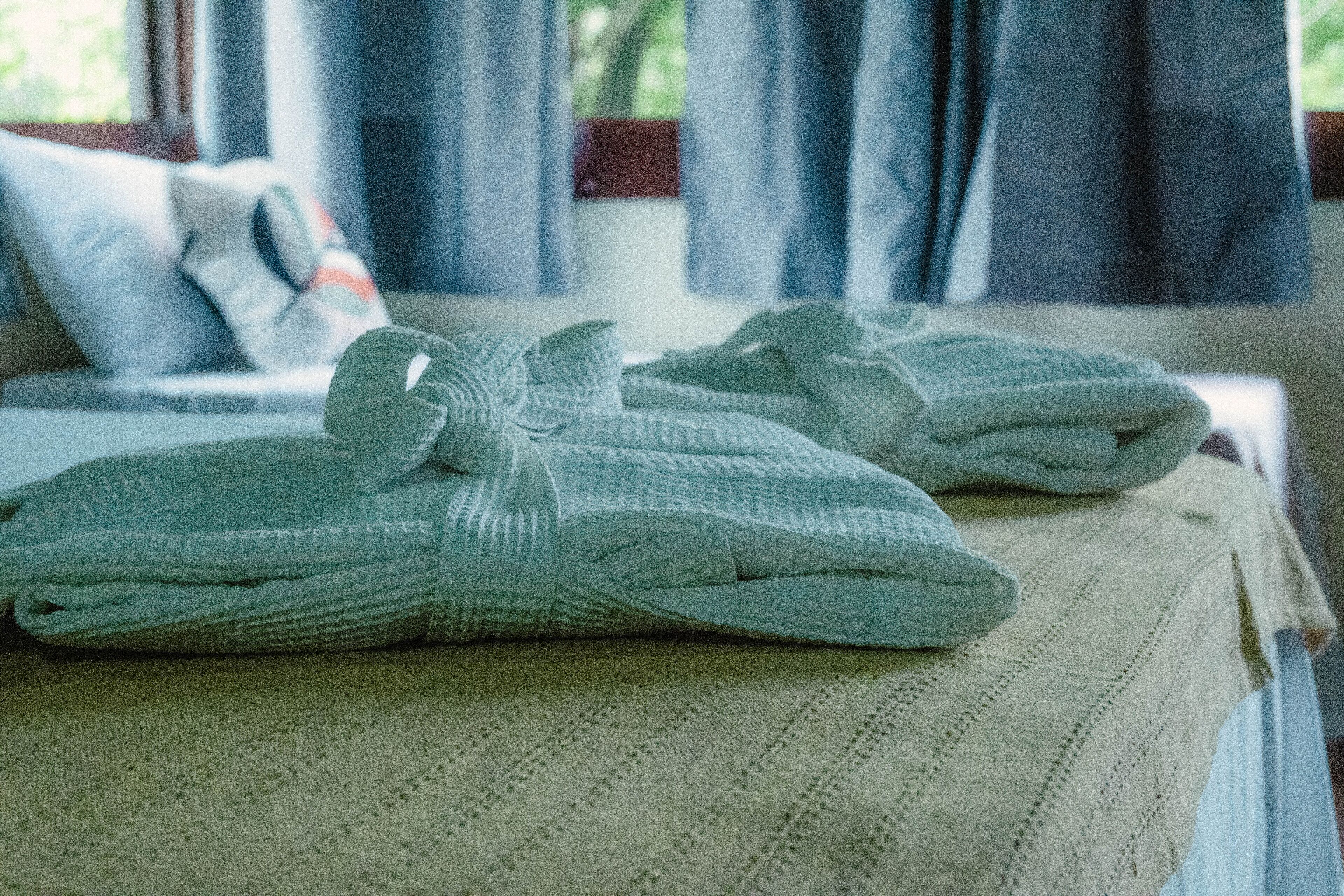 A neatly made bed with a folded towel and a pillow on a bed with a textured white bedspread.