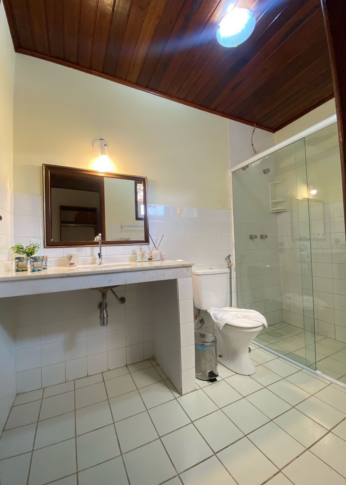 A bathroom with a wooden ceiling, a mirror, a sink, a toilet, and a glass-enclosed shower area.