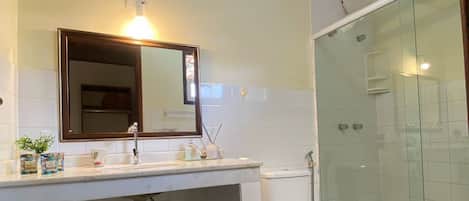 A bathroom with a wooden ceiling, a mirror, a sink, a toilet, and a glass-enclosed shower area.