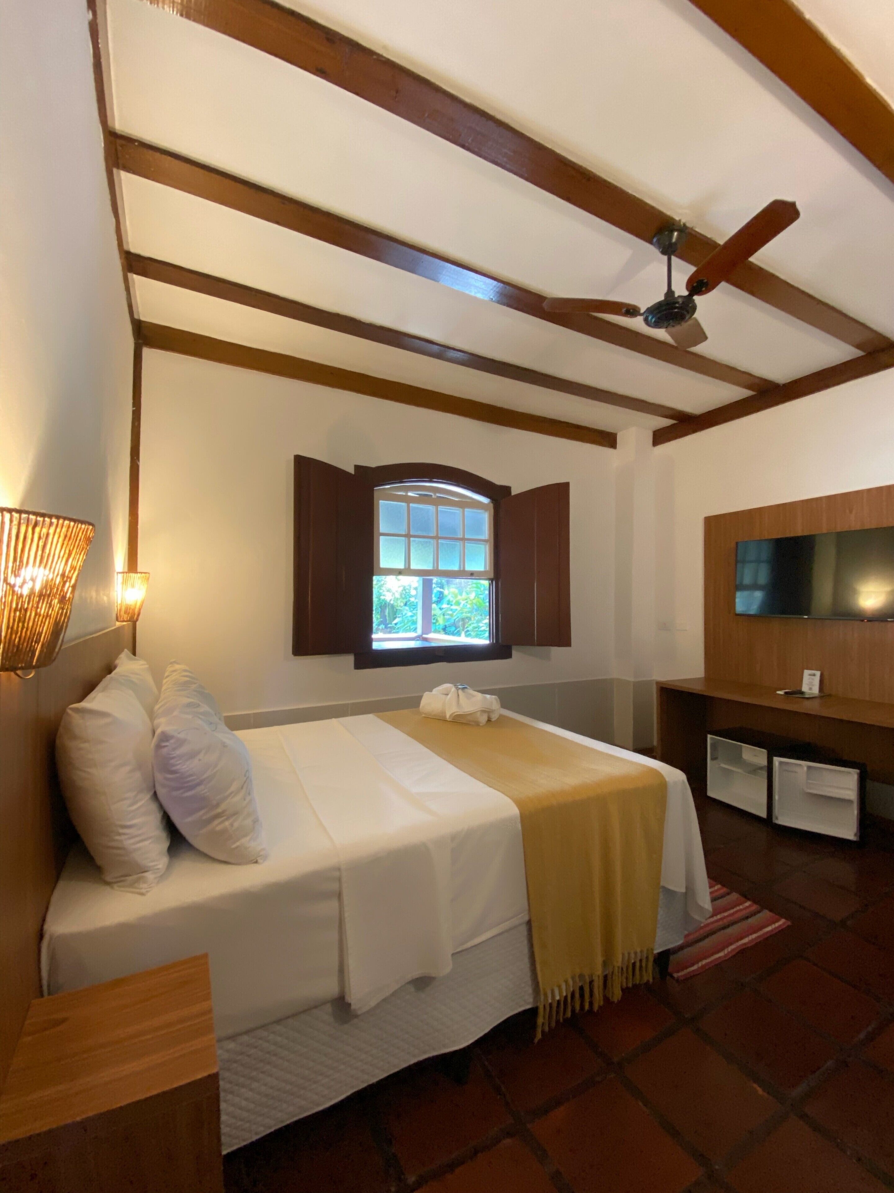 A bedroom with a bed, a window, a ceiling fan, and a TV.