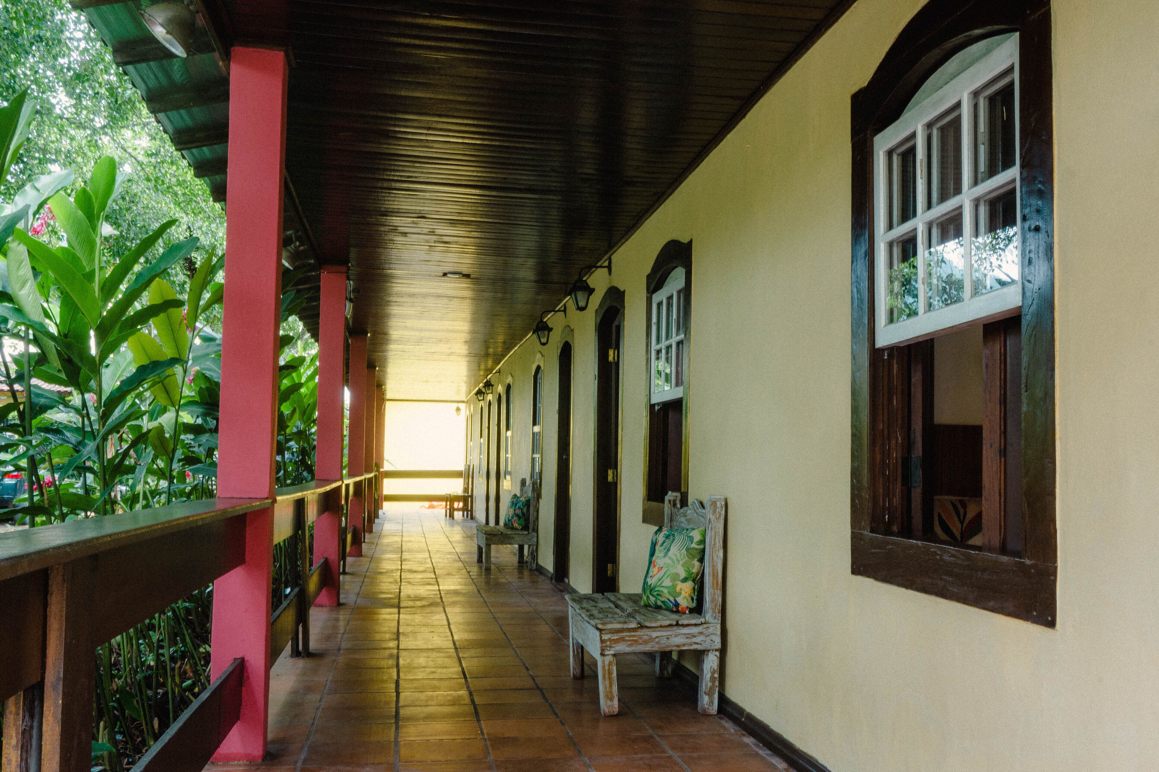A covered corridor with benches, a tiled floor, and a view of greenery outside.