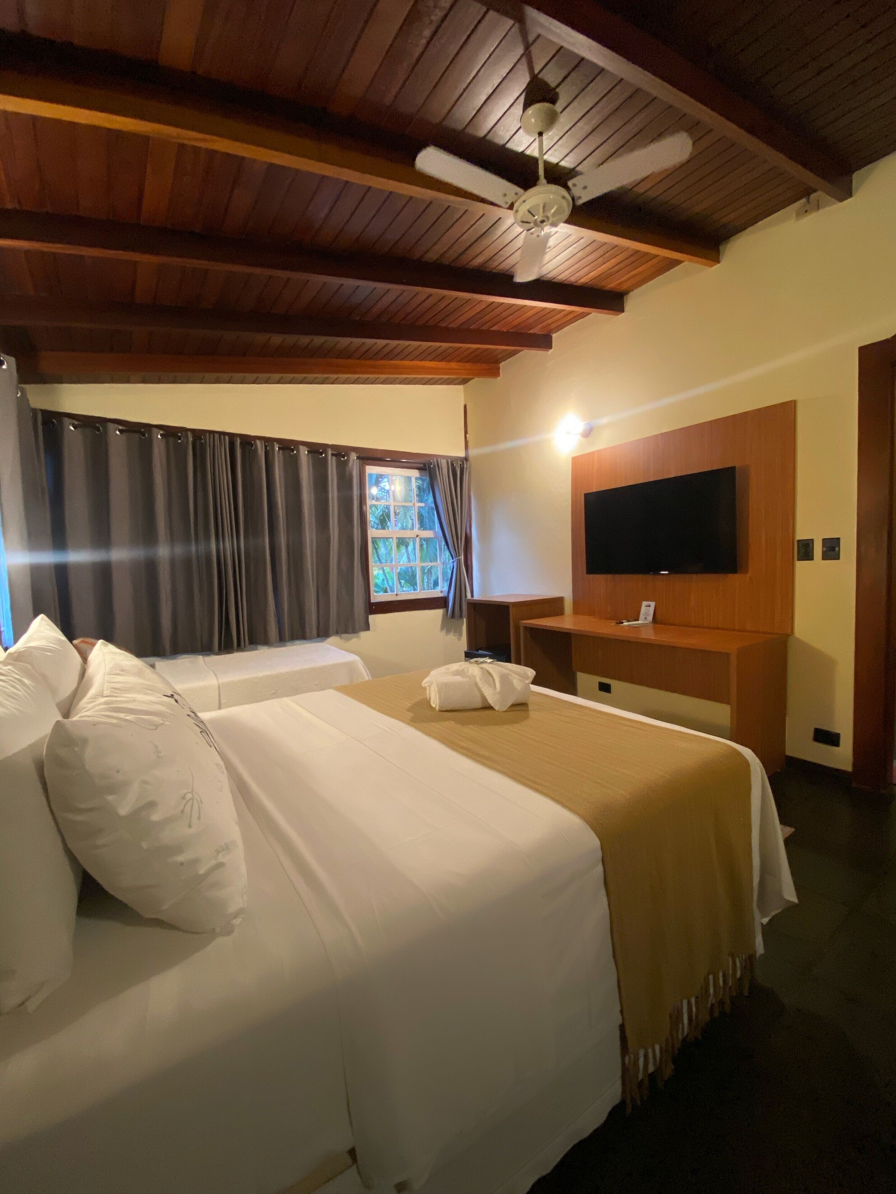 A hotel room with a bed, a desk, a television, and a window with curtains.