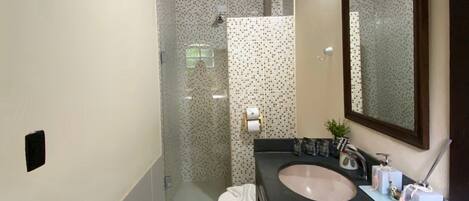 A bathroom with a wooden ceiling, a shower with a glass door, a sink with a mirror, and a toilet.