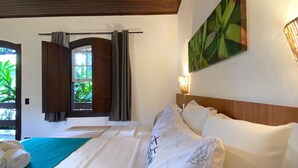 Ein Hotelzimmer mit Holzboden, einem Bett mit weißen Leinen, einem grünen Handtuch auf dem Bett, einem Fenster mit Vorhängen und einer Wandlampe.