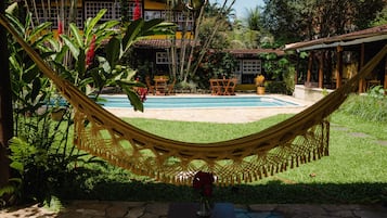 A hammock over a pool with a house in the background.