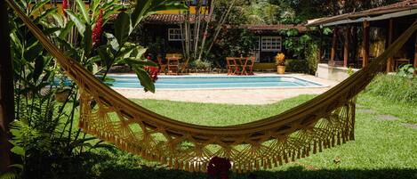 A hammock over a pool with a house in the background.