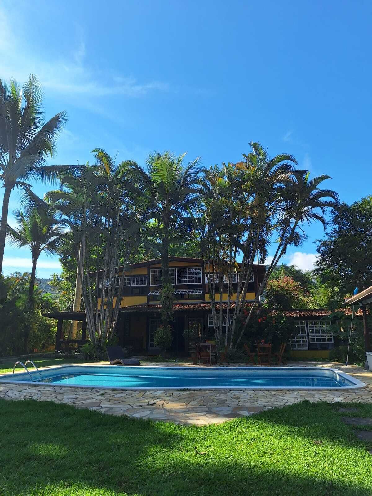 Un bâtiment à deux étages doté d’une piscine, entouré de palmiers et d’une végétation luxuriante.