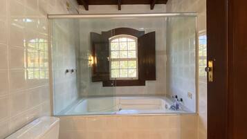 A modern bathroom with a glass-enclosed shower, a white toilet, and a wooden bench.