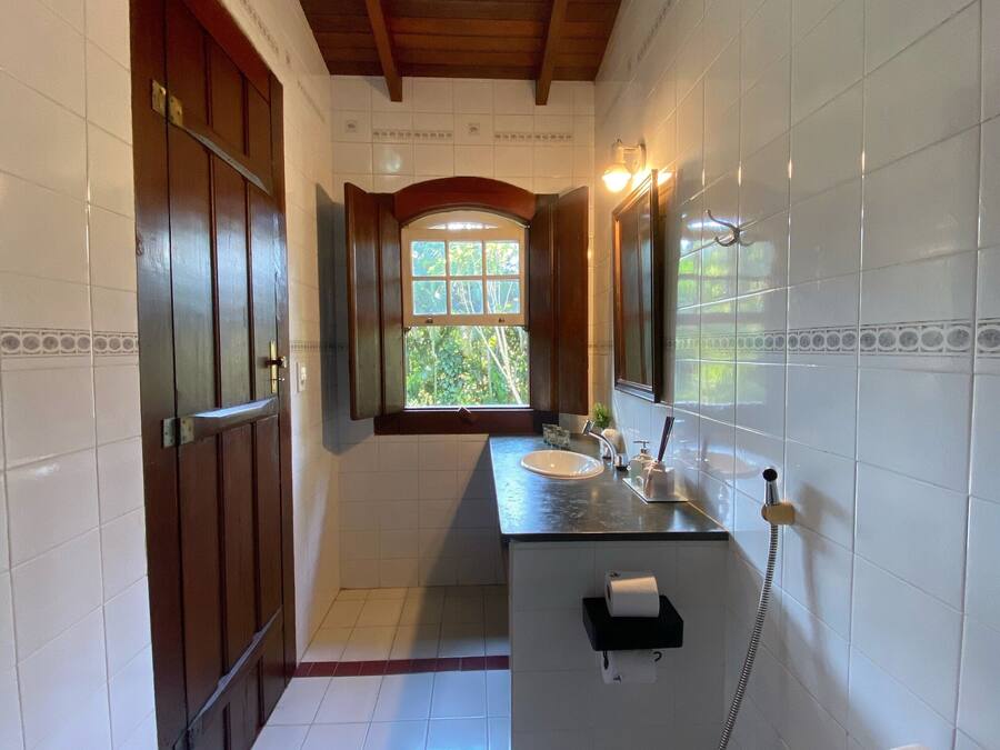 A bathroom with a wooden ceiling, white tiled walls, a window, a sink, and a toilet.