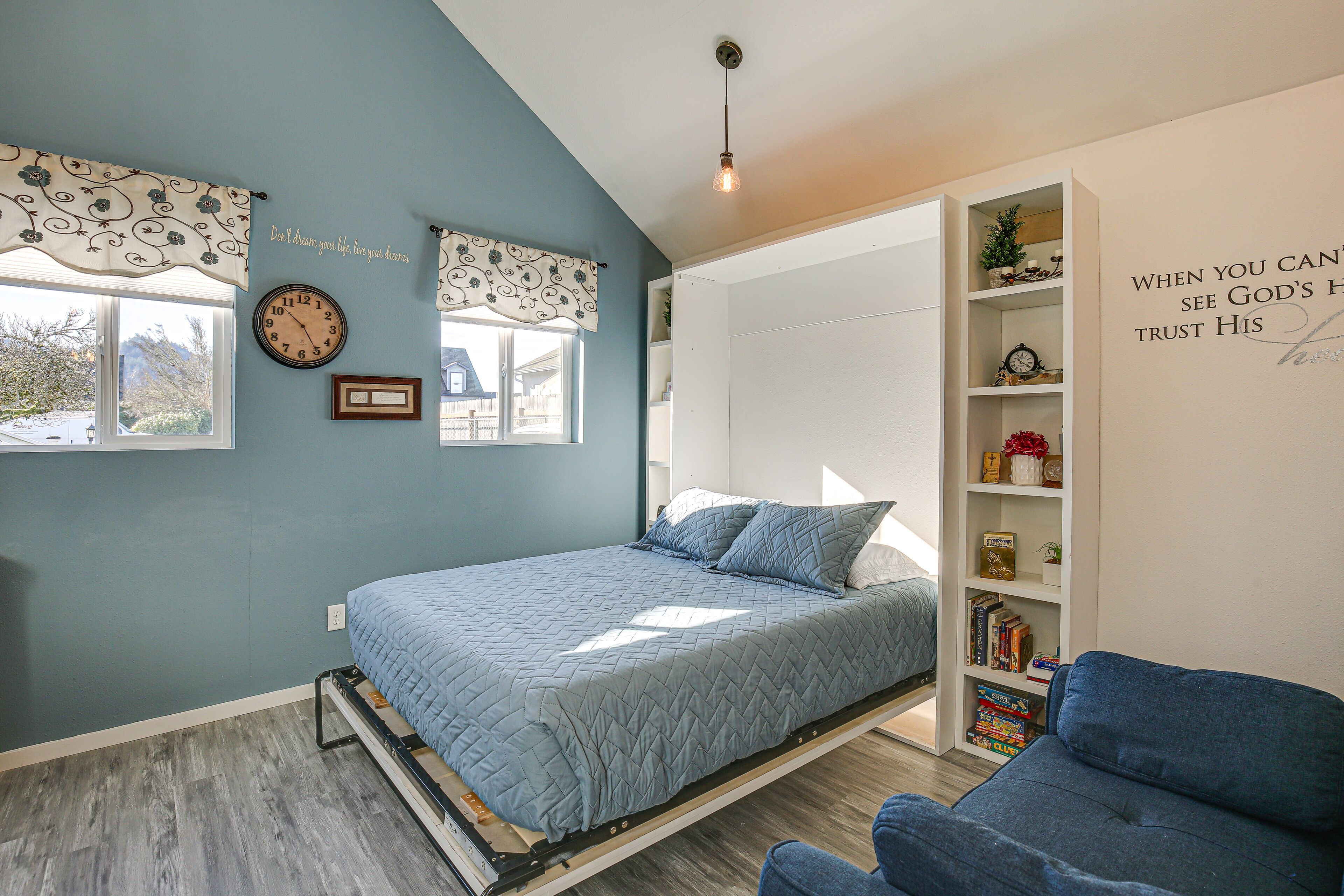 Een slaapkamer met een bed, een blauwe stoel, een boekenkast en een raam.