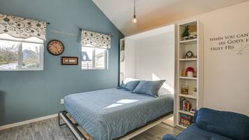 Een slaapkamer met een bed, een blauwe stoel, een boekenkast en een raam.