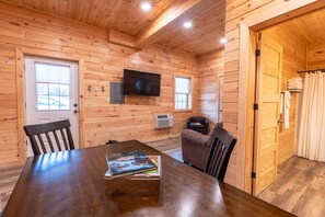 L'intérieur d'une cabane en bois comprend une table à manger, des chaises, un téléviseur fixé au mur et un petit coin salon.