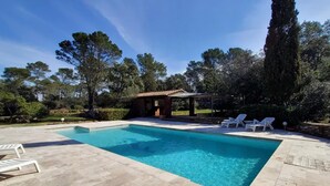 A rectangular swimming pool with clear blue water, surrounded by a stone deck. There are white lounge chairs and a small wooden structure in the background. - Domaine du Dauphin (Cuers)