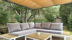 A covered outdoor seating area with a beige canopy, a beige sectional sofa, and a wooden coffee table. - Domaine du Dauphin (Cuers)