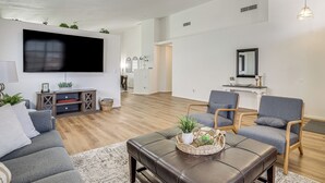 A modern living room with a flat-screen TV, grey sofas, a leather ottoman, and wooden flooring. - Las Vegas Home w/ Covered Patio ~ 5 Mi to Strip! (Las Vegas)