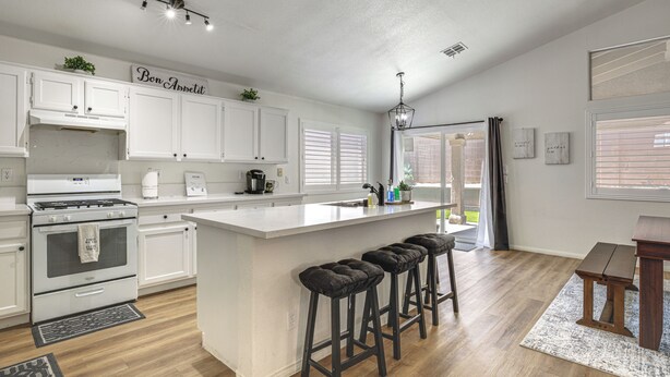 A modern kitchen with white cabinetry, a central island with stools, a built-in oven, and a dining area with a bench. - Las Vegas Home w/ Covered Patio ~ 5 Mi to Strip! (Las Vegas)