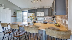 A kitchen with dark cabinets, a white refrigerator, a microwave, and a sink. There are four wooden chairs around a central island with a bowl of fruit. - Village of Four Seasons Lake Condo w/ Pool Access! (Village of Four Seasons)