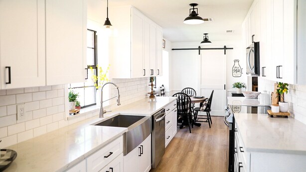 A modern kitchen with white cabinetry, a wooden floor, and a dining area with black chairs. - New Year’s Retreat. Cozy Modern Farmhouse! Close to historic downtown Wylie! (Wylie)