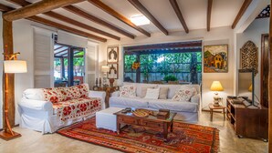 A cozy living room with a white sofa, a wooden coffee table, and a large window with a view of greenery. - Casa Amendoeiras Charme e Conforto à Beira-mar (Ponta de Serrambi Ipojuca)