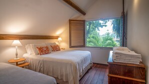 A bedroom with a bed, bedside tables, a window with blinds, and a stack of towels. - Casa Amendoeiras Charme e Conforto à Beira-mar (Ponta de Serrambi Ipojuca)