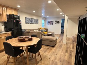 A modern kitchen with a dining area, a living room with a sofa and coffee table, and a hallway leading to another room.