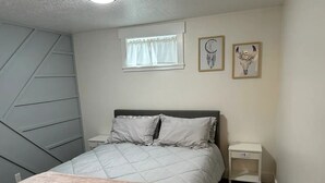 Une chambre à coucher avec un lit, des tables de chevet, une fenêtre avec des rideaux et des œuvres d’art murales.