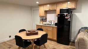 Une cuisine de taille réduite, dotée de meubles de rangement en bois, d’un réfrigérateur noir et d’une table à manger avec des chaises.
