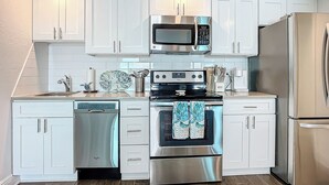 Cocina moderna con armarios blancos, electrodomésticos de acero inoxidable, incluyendo microondas, horno y refrigerador, además de lavavajillas.