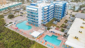 Un hotel de varios pisos con zona de piscina, que incluye tumbonas y sombrillas.