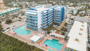 Un hotel de varios pisos con piscina en la azotea y otra piscina separada.
