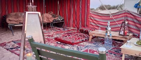 A tented area with a patterned carpet, a wooden table with bottles, and a bench.