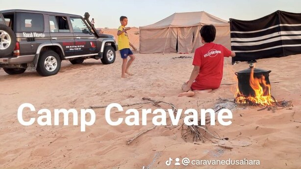 A desert campsite with a caravan, tents, and a fire.