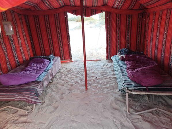 Una tienda de campaña con dos camas, cada una con una manta y almohadas a rayas.