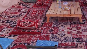 A room with a wooden table, patterned rugs, and a blue polka dot chair.
