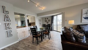 Een moderne keuken met witte kastjes, een eethoek met een glazen tafel en stoelen, en een woonkamer met een leren bank.